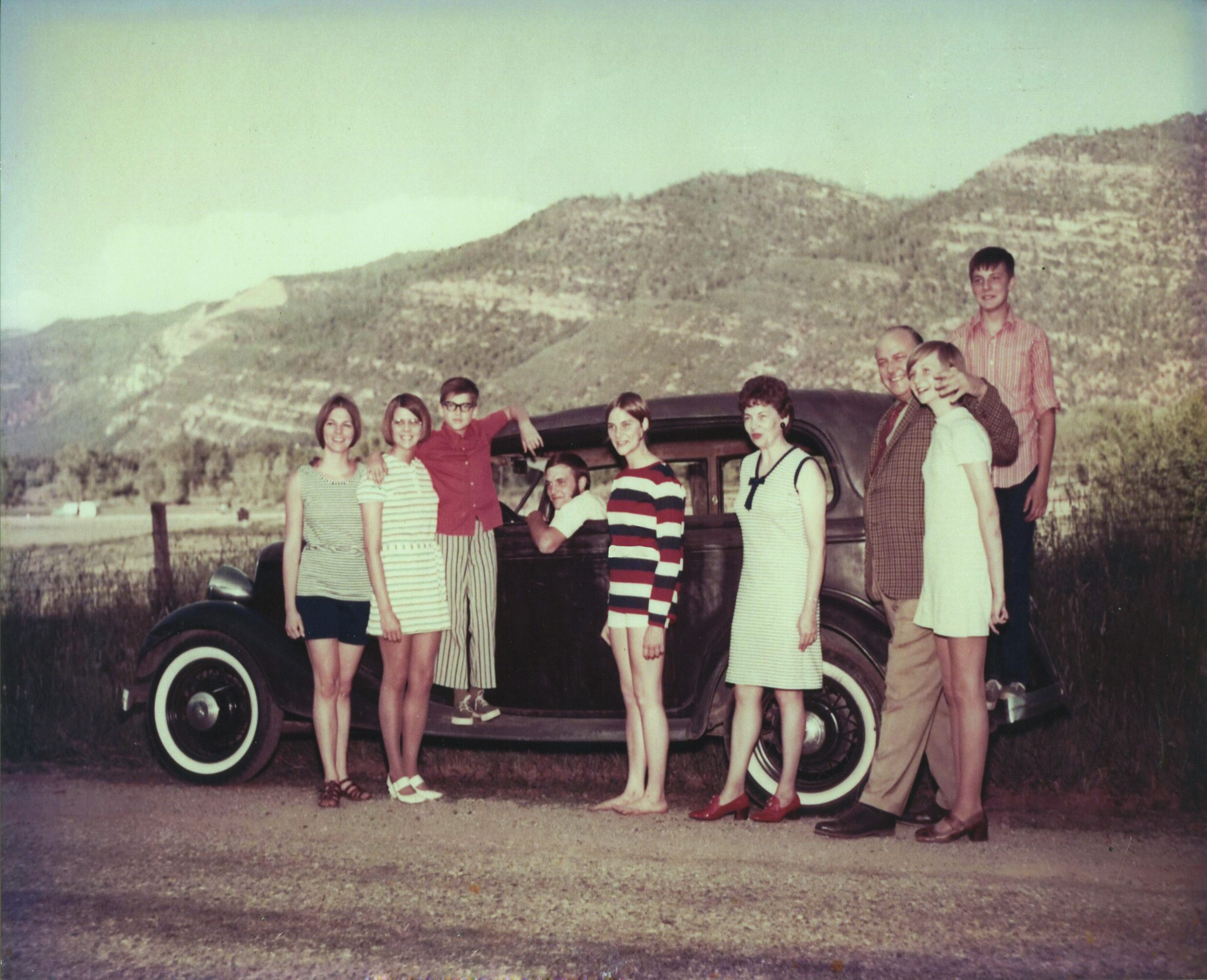 group of people standing near a old car