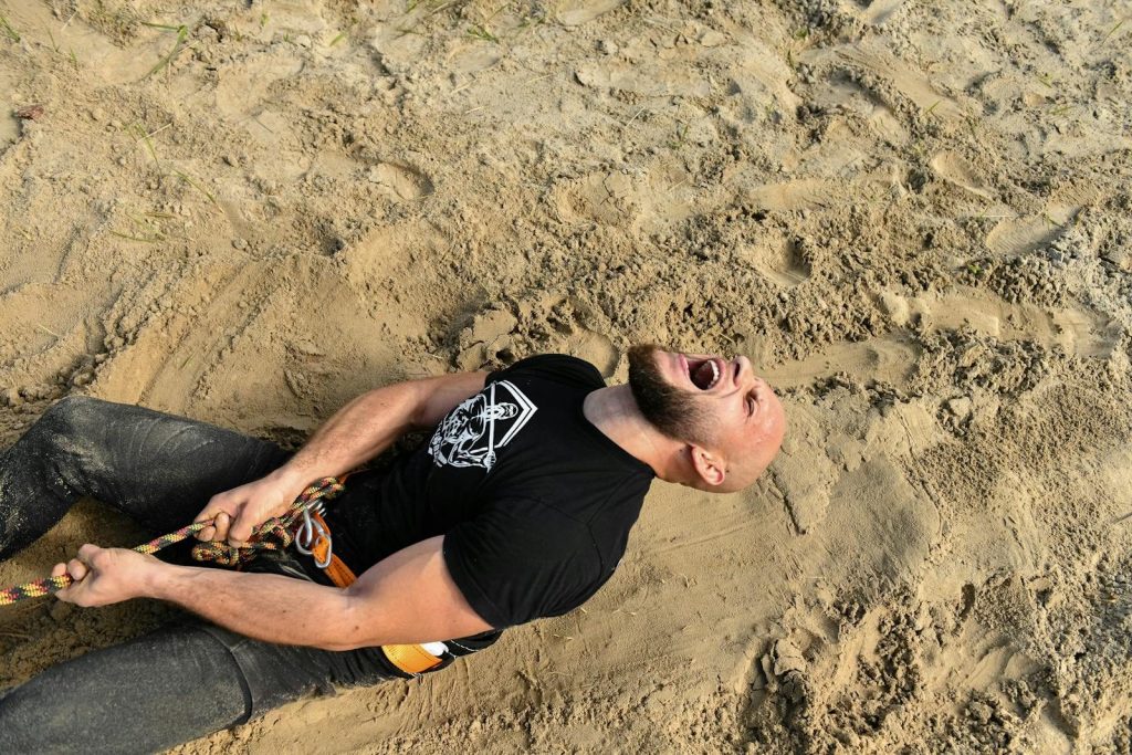 Man exerting strength in intense tug of war, showcasing determination in a sandy setting.